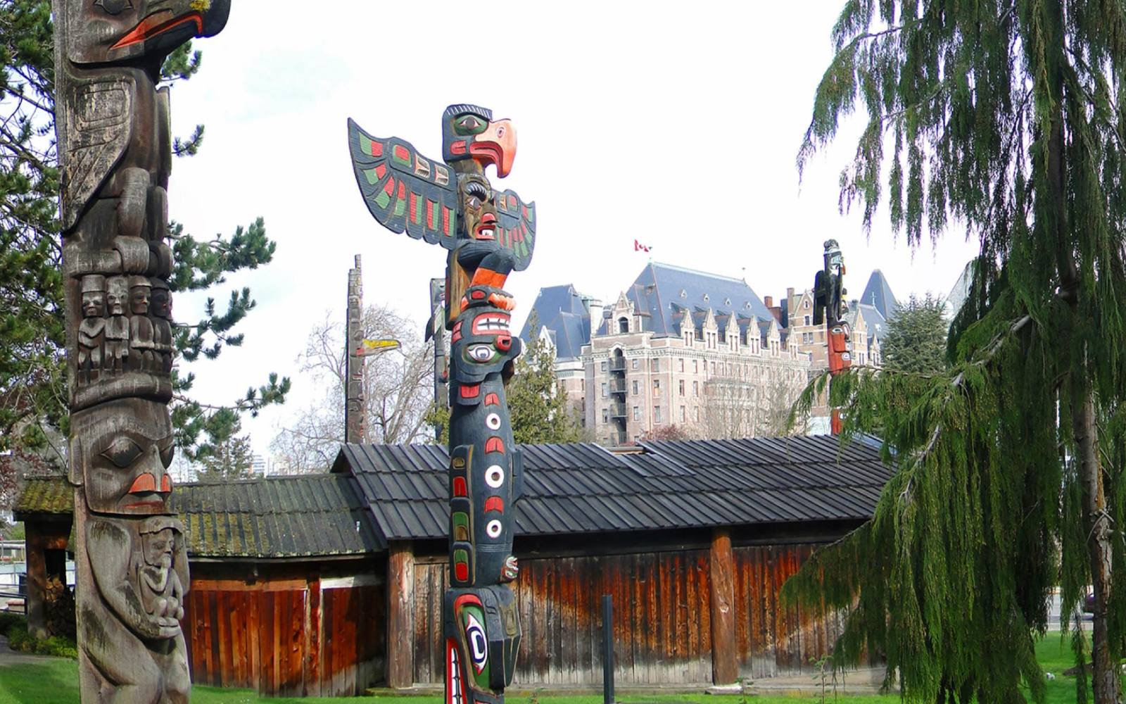 the totem poles at thunderbird park with the empress hotel in the background for an article on the top free things to do in victoria.