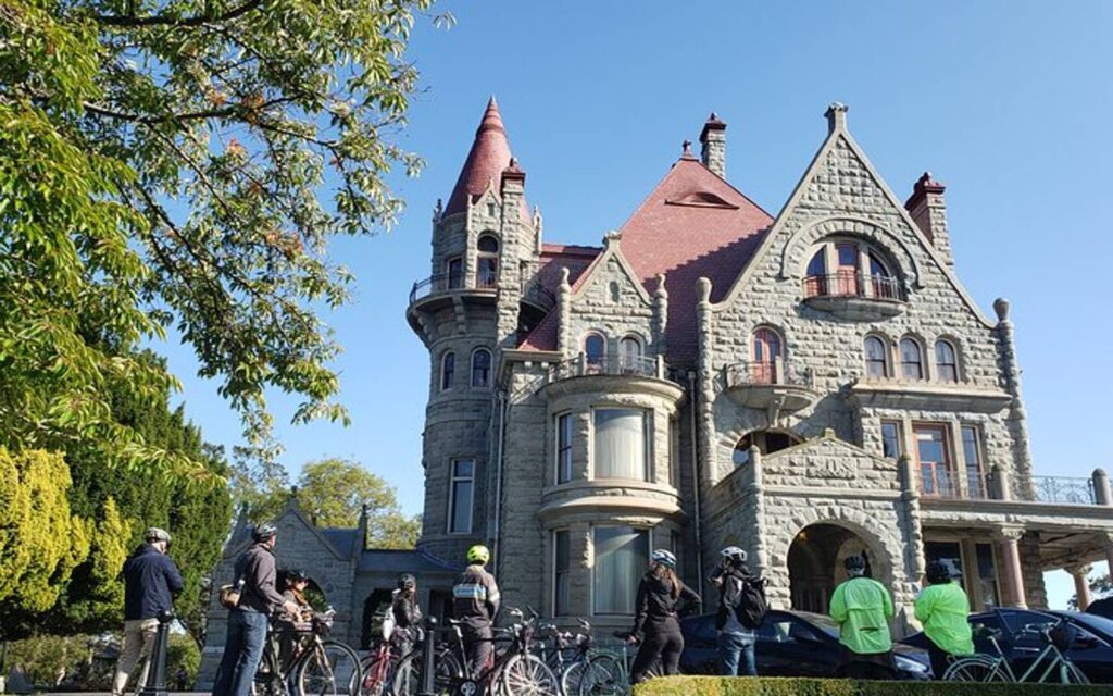 a group stands in front of craigdarroch castle on a victoria bike tour